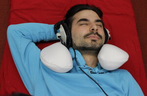Ein Mann liegt auf seinem Bett und hört mit Kopfhörern Musik zum Einschlafen.